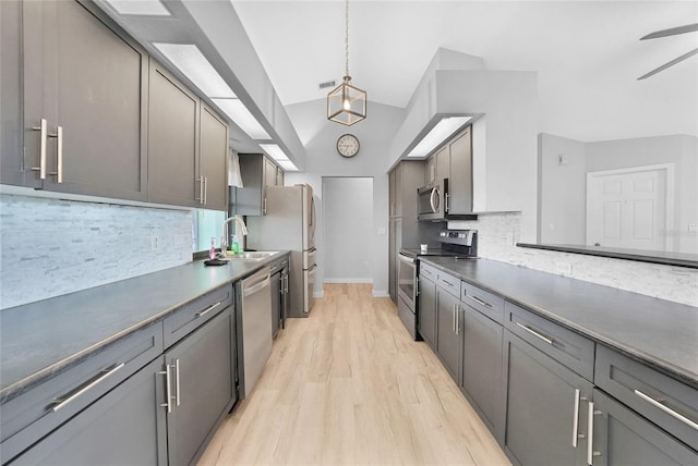 kitchen featuring stainless steel appliances, light wood-style flooring, a sink, tasteful backsplash, and dark countertops