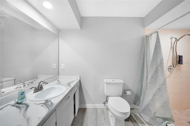 bathroom with toilet, a stall shower, vanity, wood finished floors, and baseboards