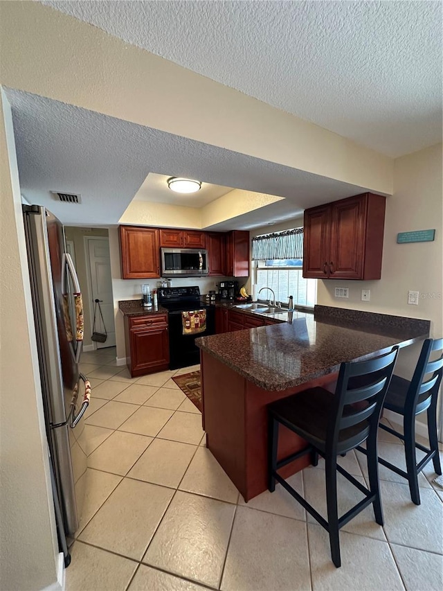 kitchen featuring a peninsula, a textured ceiling, stainless steel appliances, and visible vents