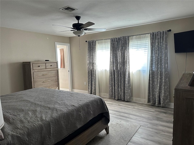 bedroom featuring a ceiling fan, a textured ceiling, baseboards, light wood finished floors, and visible vents