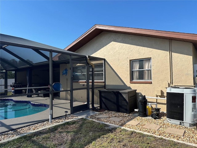 rear view of house featuring a patio, stucco siding, glass enclosure, and an outdoor pool