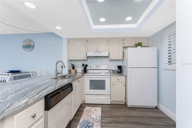 kitchen with a sink, white appliances, under cabinet range hood, dark wood-style floors, and a tray ceiling
