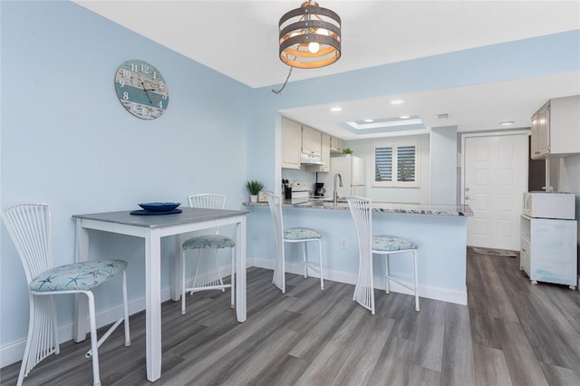 kitchen with a peninsula, a kitchen bar, baseboards, and dark wood finished floors