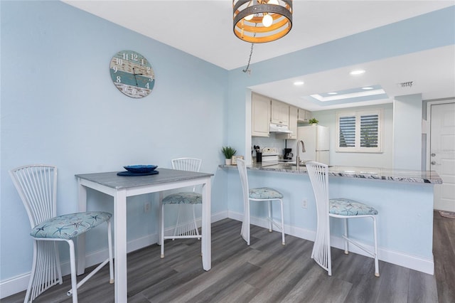 kitchen with dark wood-style flooring, a kitchen breakfast bar, and baseboards