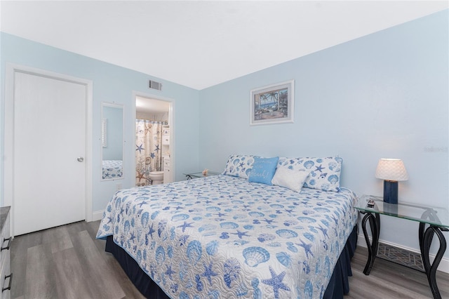 bedroom with connected bathroom, visible vents, wood finished floors, and baseboards