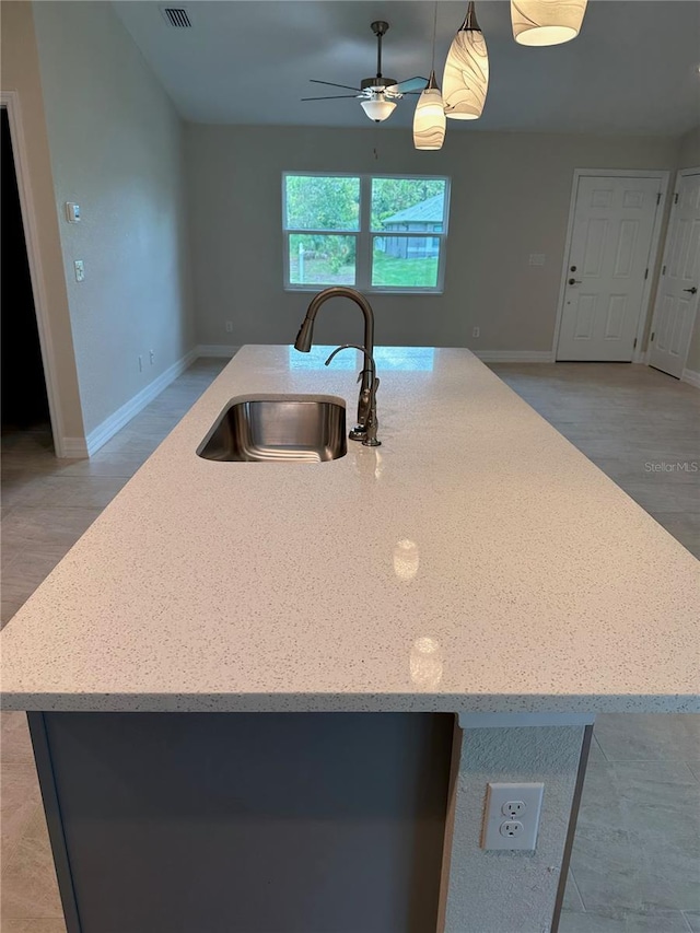 kitchen with a sink, a center island with sink, open floor plan, hanging light fixtures, and baseboards