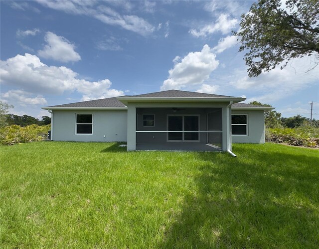 back of property with a sunroom, stucco siding, and a yard