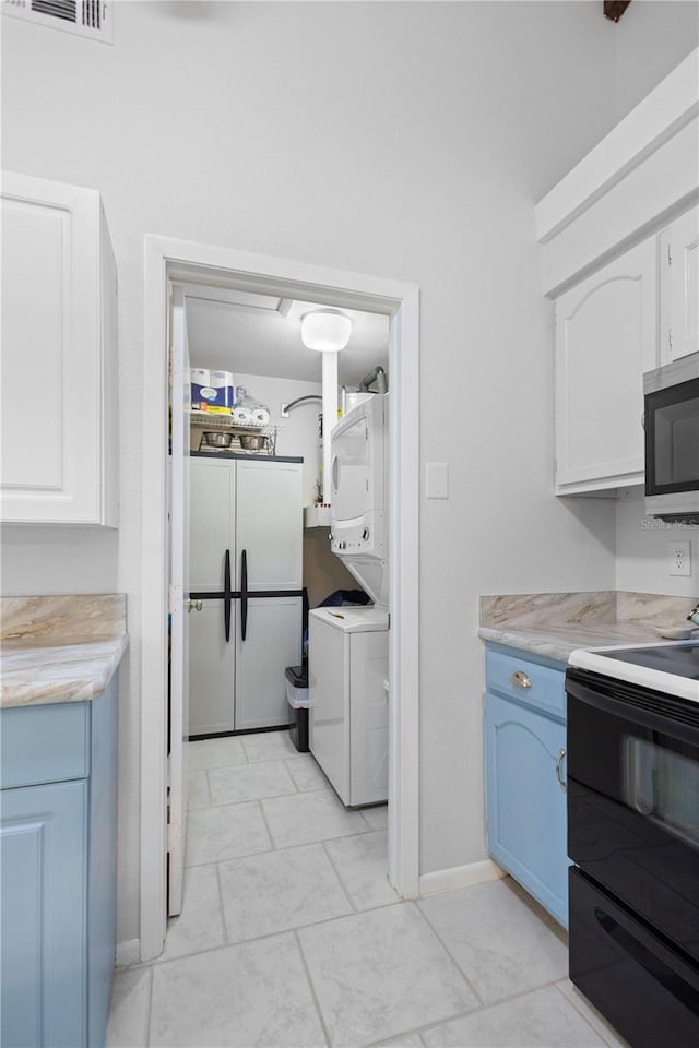 5301 Linksman Pl, North Port, FL 34287 - kitchen with stacked washer / dryer, black / electric stove, stainless steel microwave, light countertops, and white cabinetry