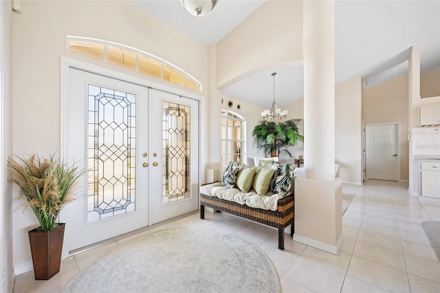 foyer entrance with a chandelier, french doors, light tile patterned floors, high vaulted ceiling, and arched walkways
