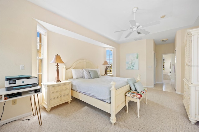 bedroom with light colored carpet, multiple windows, a tray ceiling, and baseboards