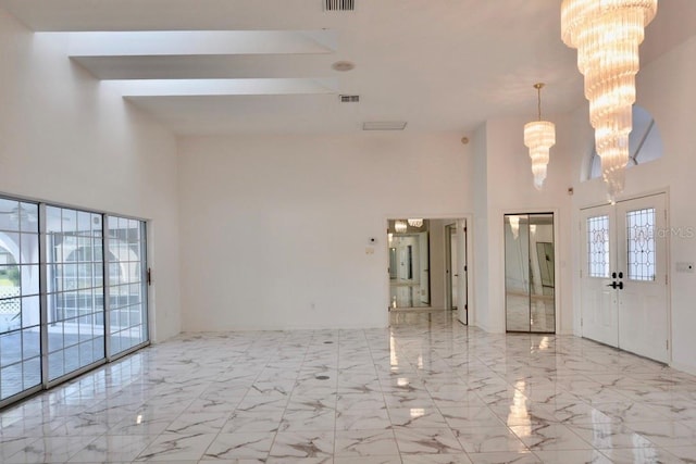 unfurnished room with a towering ceiling, a chandelier, and marble tiled flooring