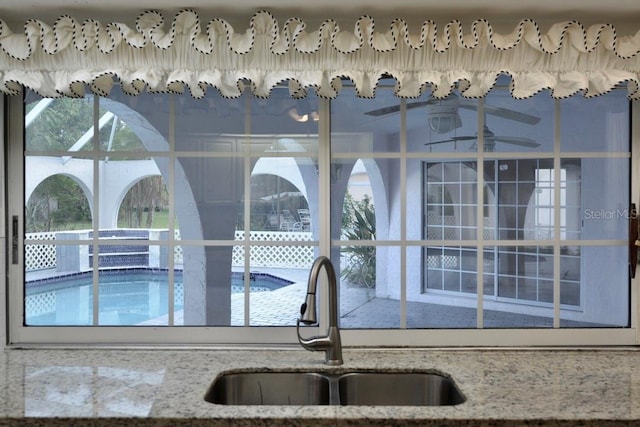 kitchen view of a sink, a swimming pool, and light stone counters