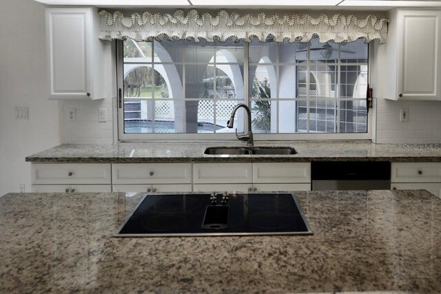 kitchen with a sink, black electric stovetop, white cabinetry, backsplash, and light stone counters