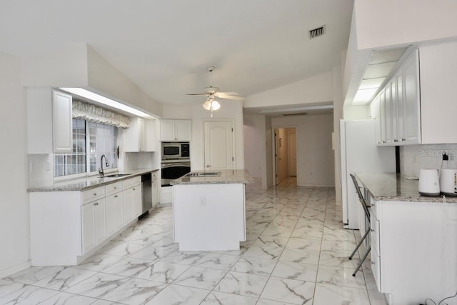 kitchen with stainless steel appliances, a sink, a center island, decorative backsplash, and white cabinets