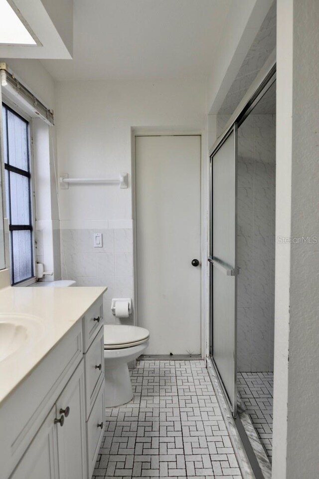 bathroom featuring a stall shower, toilet, vanity, and brick patterned flooring