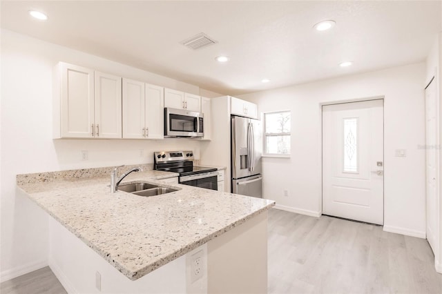 27438 Corinthian Dr, Punta Gorda, FL 33955 - kitchen featuring appliances with stainless steel finishes, a sink, light wood-style floors, light stone countertops, and white cabinets
