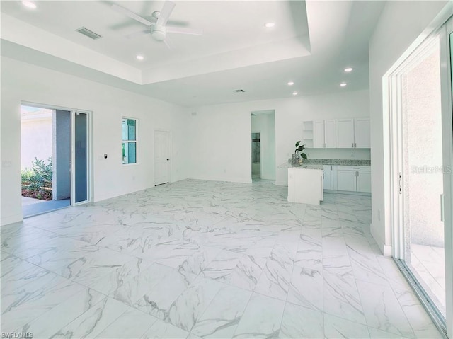 unfurnished living room with a tray ceiling, recessed lighting, ceiling fan, and light marble finish floors