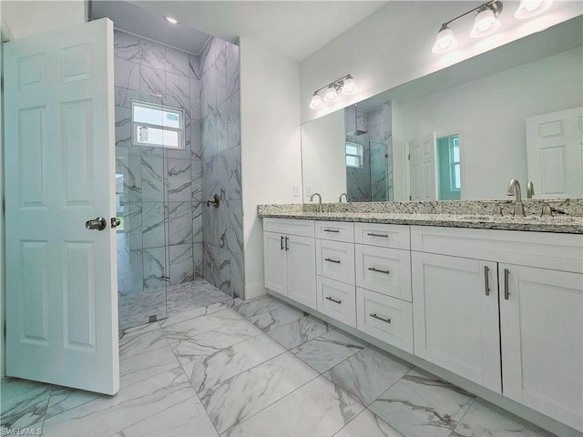bathroom featuring marble look tile flooring, a marble finish shower, double vanity, and baseboards
