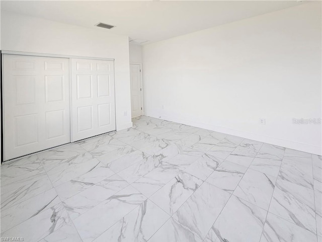 unfurnished bedroom featuring a closet, light marble finish floors, and baseboards