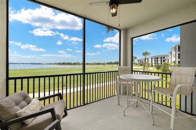 sunroom featuring a ceiling fan, a water view, and golf course view