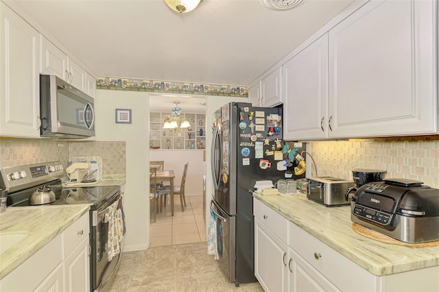 12018 Saragossa Ln, North Port, FL 34287 - kitchen with stainless steel appliances, a chandelier, white cabinetry, backsplash, and light stone counters