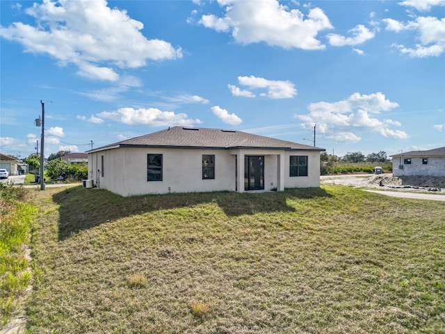 back of property with stucco siding, a yard, and central AC