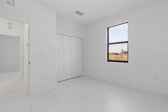 unfurnished bedroom featuring marble finish floors, baseboards, and a closet