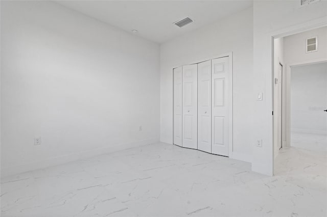 unfurnished bedroom featuring light marble finish floors, a closet, and baseboards