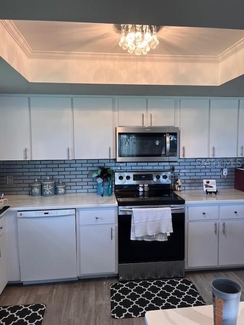 kitchen featuring stainless steel appliances, ornamental molding, wood finished floors, light countertops, and white cabinetry