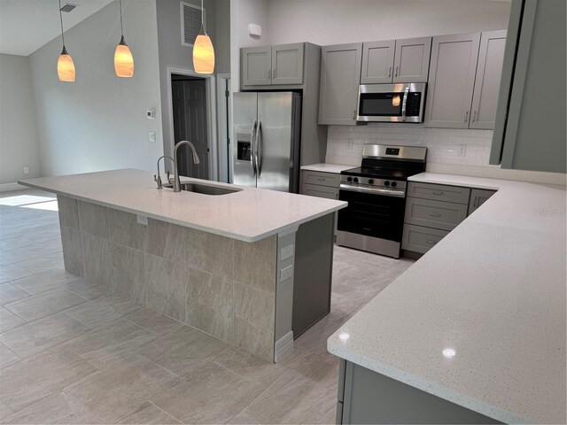 kitchen featuring appliances with stainless steel finishes, a sink, gray cabinetry, backsplash, and light stone counters