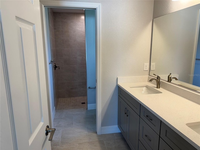 full bath with a tile shower, double vanity, a textured wall, baseboards, and tile patterned floors