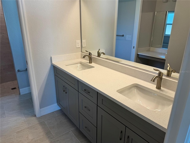 bathroom featuring double vanity, tile patterned flooring, baseboards, and a tile shower