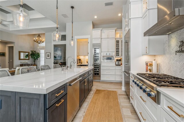 1306 Osprey Dr, Punta Gorda, FL 33950 - kitchen featuring wall chimney range hood, appliances with stainless steel finishes, white cabinets, a sink, and decorative backsplash