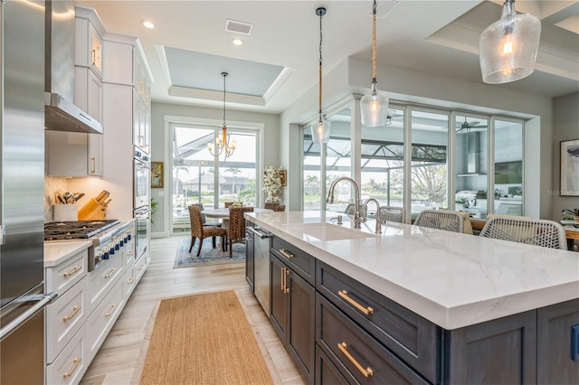 1306 Osprey Dr, Punta Gorda, FL 33950 - kitchen featuring a raised ceiling, a sink, stainless steel appliances, white cabinets, and an island with sink