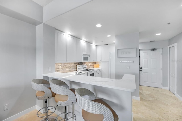 kitchen with white appliances, tasteful backsplash, baseboards, a breakfast bar, and recessed lighting
