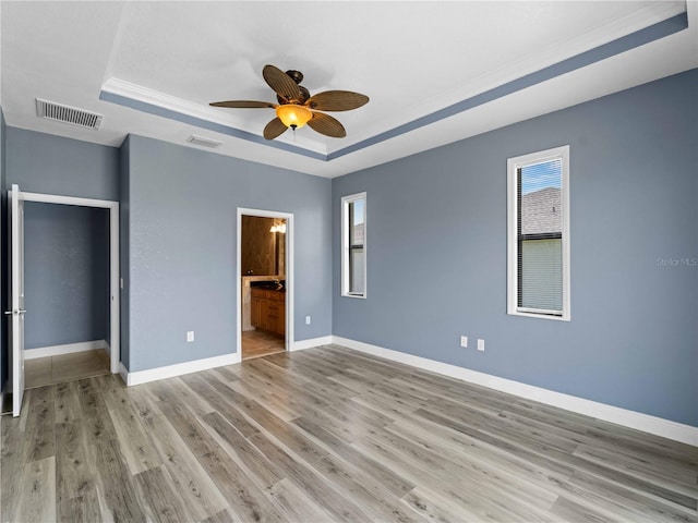 97 Pine Valley Ln, Rotonda West, FL 33947 - unfurnished bedroom featuring a raised ceiling, baseboards, light wood-style floors, connected bathroom, and crown molding