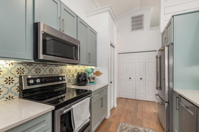kitchen featuring appliances with stainless steel finishes, ornamental molding, light wood-style floors, backsplash, and light stone counters