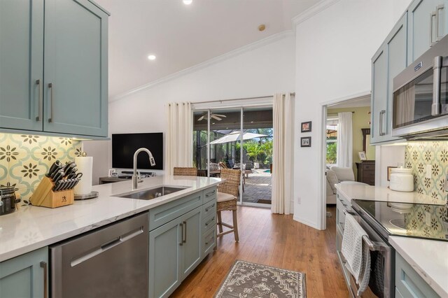 kitchen featuring stainless steel appliances, a sink, tasteful backsplash, ornamental molding, and light wood finished floors