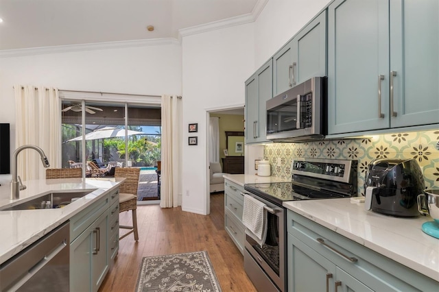 kitchen with stainless steel appliances, a sink, ornamental molding, backsplash, and light wood-type flooring