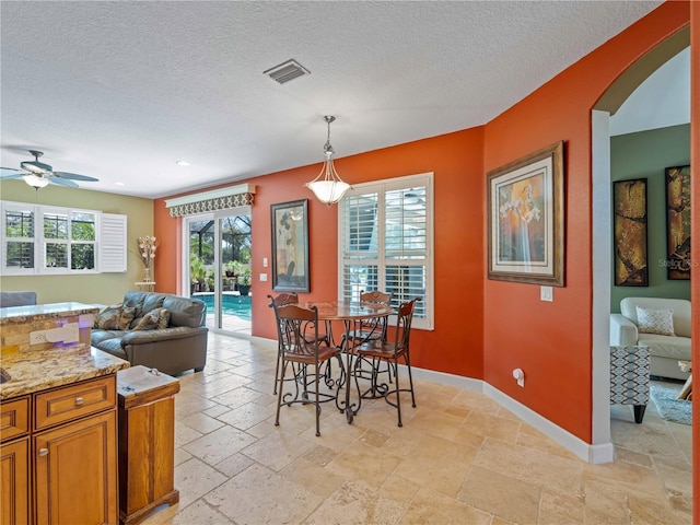 11982 Granite Woods Loop, Venice, FL 34292 - dining room featuring stone tile flooring, baseboards, a textured ceiling, a ceiling fan, and arched walkways