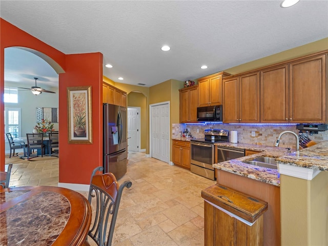 11982 Granite Woods Loop, Venice, FL 34292 - kitchen featuring stainless steel appliances, a sink, arched walkways, brown cabinetry, and ceiling fan