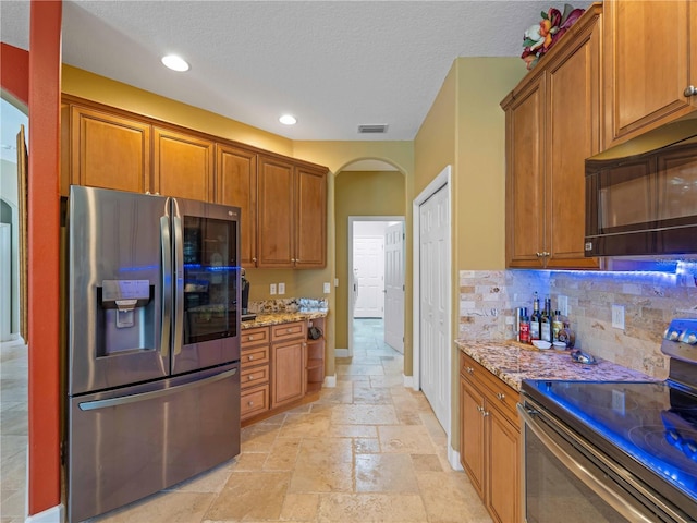 11982 Granite Woods Loop, Venice, FL 34292 - kitchen with stainless steel appliances, arched walkways, stone tile flooring, light stone countertops, and brown cabinets