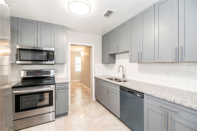 kitchen with stainless steel appliances, a sink, gray cabinets, backsplash, and baseboards
