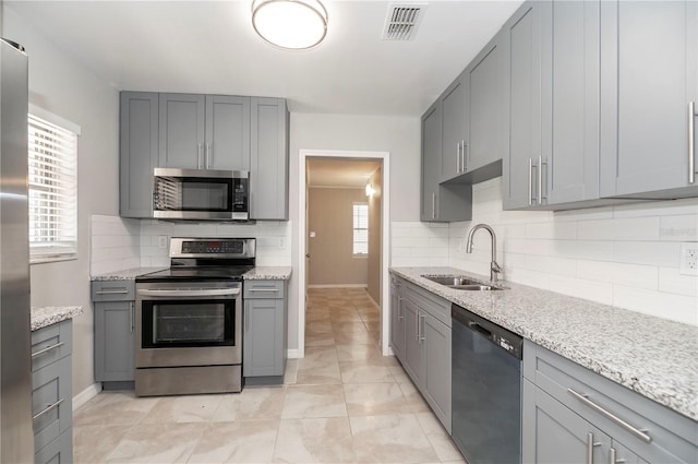 kitchen with appliances with stainless steel finishes, a sink, gray cabinetry, and backsplash