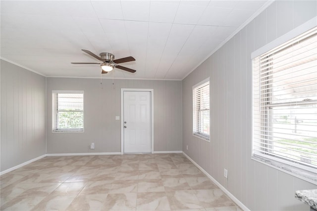 unfurnished room with ornamental molding, a ceiling fan, baseboards, and wooden walls