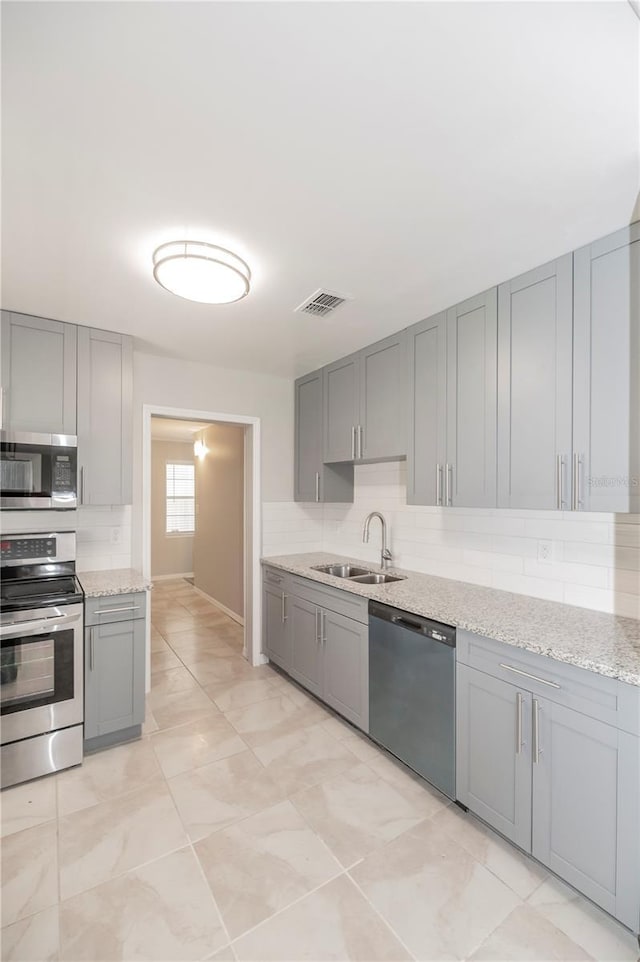 kitchen featuring stainless steel appliances, a sink, gray cabinets, and decorative backsplash