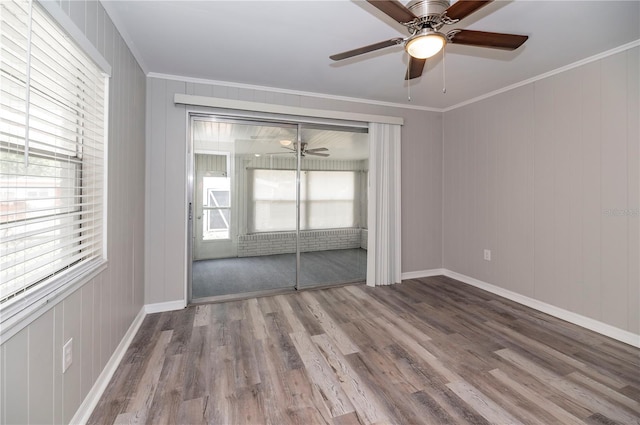 spare room featuring ceiling fan, plenty of natural light, wood finished floors, baseboards, and ornamental molding