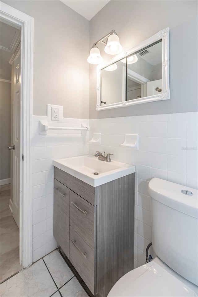 bathroom with tile walls, toilet, wainscoting, vanity, and marble look tiles