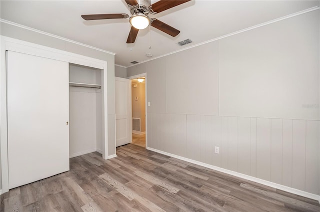 unfurnished bedroom with wood finished floors, crown molding, a closet, a ceiling fan, and baseboards