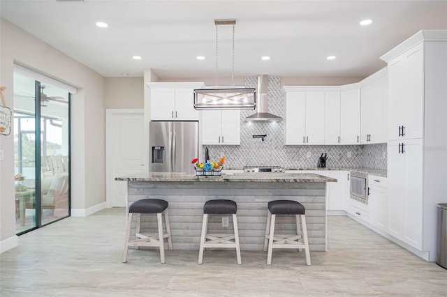 kitchen with appliances with stainless steel finishes, wall chimney range hood, backsplash, a kitchen island, and a breakfast bar area